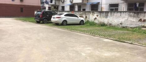 A parking area with two cars, a concrete surface, and a low wall with a small grassy area beside it.