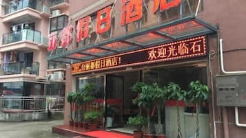 A hotel entrance with a red carpet, potted plants, and a digital signboard.