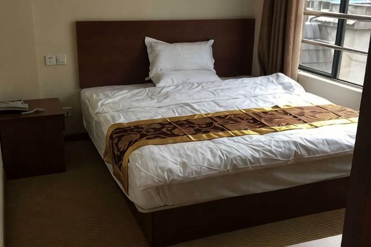 A hotel room with a bed, a nightstand, a window, and a view of the outside.