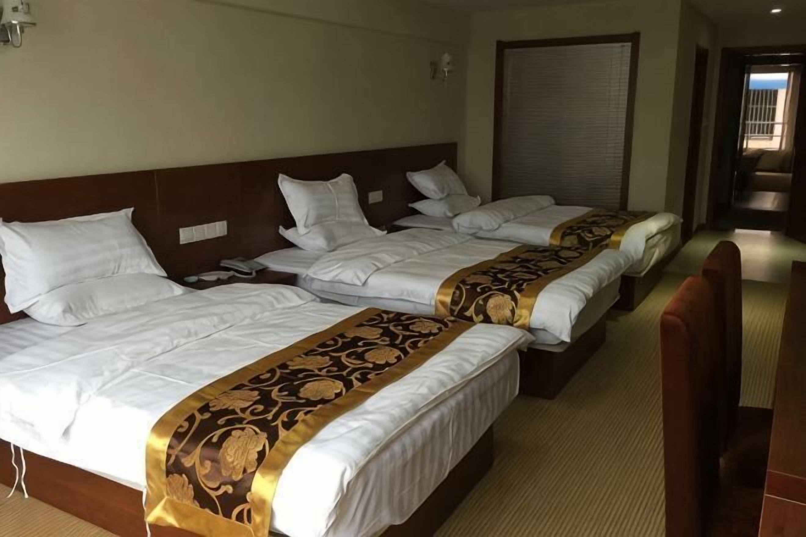 Habitación de hotel con tres camas, cabecera de madera, teléfono y puerta cerrada.