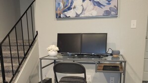 Un espai de treball a casa amb escriptori, dos monitors, una cadira i un quadre decoratiu.