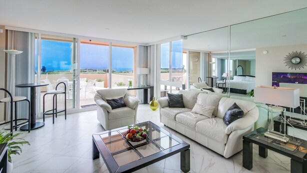 Een moderne woonkamer met een glazen salontafel, witte banken en uitzicht op de zee.