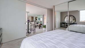 Een moderne slaapkamer met een groot bed, een spiegel en uitzicht op de woonkamer.