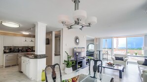 Een moderne keuken met witte kasten, een centraal eiland en een eethoek met een glazen tafel en stoelen.