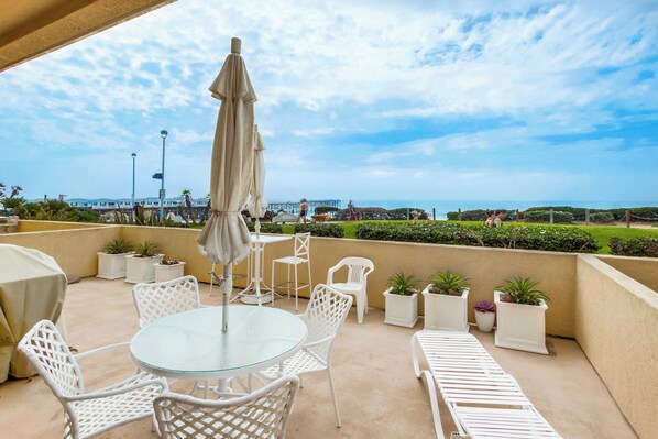 Eine Terrasse mit Glastisch und weißen Stühlen, umgeben von Blumentöpfen und Blick aufs Meer.