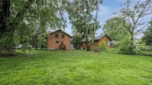 Una casa a due piani con un prato curato e alberi grandi nel giardino.