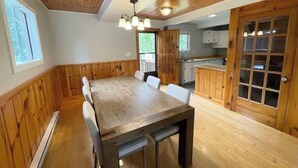 Zona pranzo con tavolo e sedie in legno, cucina con mobili in legno e un'ampia finestra.