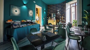 Comedor con paredes verde azulado, una mesa de buffet y varias mesas con sillas.