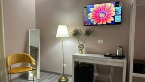 Una habitación con escritorio, silla, lámpara, un espejo grande y televisión en la pared.