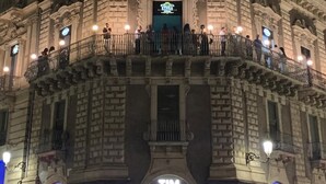 Edificio histórico con arquitectura ornamentada, una entrada destacada y un balcón con gente.