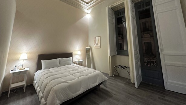 Un dormitorio con una cama grande, dos lámparas de noche, una mesita de noche, un espejo y una puerta que da a un balcón.