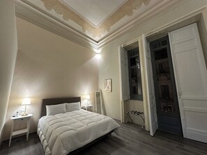 Un dormitorio con una cama grande, dos lámparas de noche, una mesita de noche, un espejo y una puerta que da a un balcón.