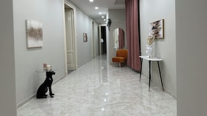 Un pasillo con piso de mármol, una estatua de perro negro, una mesita con cubierta de vidrio y una silla.