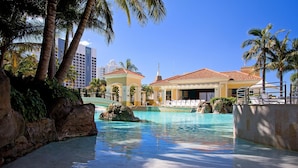 A resort pool area with clear water, palm trees, and a building with a red-tiled roof. - 2 Bed 1 Bath Apartment at Chevron - Q Stay (CHEV 3107 - 2N - NB) (Surfers Paradise)