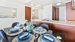 A modern kitchen with a central island, a dining area with blue plates and woven placemats, and a large mirror on the wall. - 2 Bed 1 Bath Apartment at Chevron - Q Stay (CHEV 3107 - 2N - NB) (Surfers Paradise)