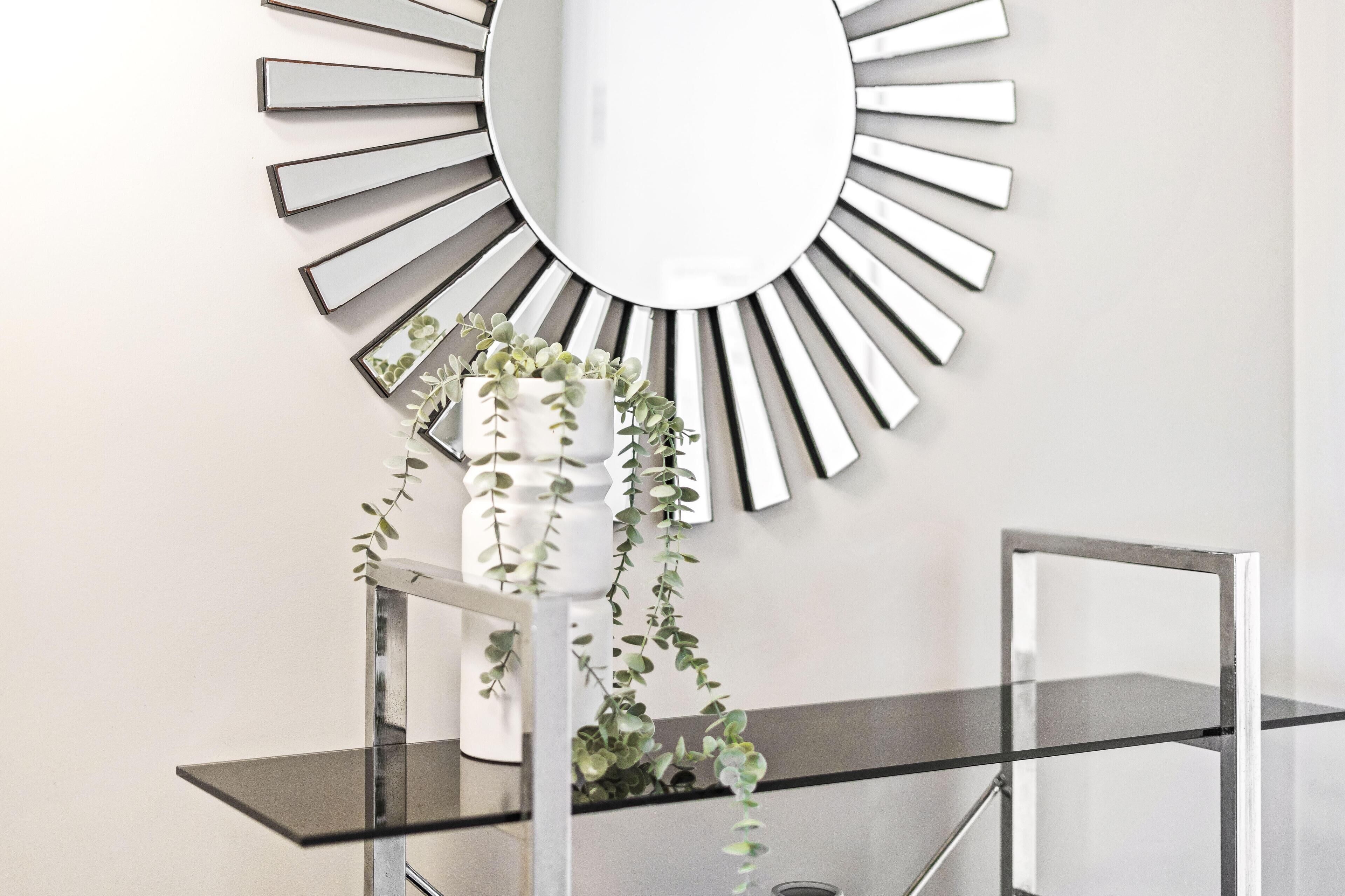 A modern interior with a sunburst mirror, a glass shelf with plants, and a metal frame structure.