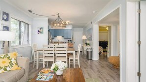 A modern living room with a wooden coffee table, a sofa, and a dining area with a chandelier. - Tennis Villa F20 - Close to Beach (Hilton Head Island)
