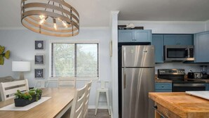 A modern kitchen with a stainless steel refrigerator, a microwave, and a stove. There is a wooden dining table with chairs and a pendant light above it. - Tennis Villa F20 - Close to Beach (Hilton Head Island)
