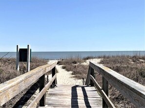 A wooden boardwalk leading to a beach with a clear sky.