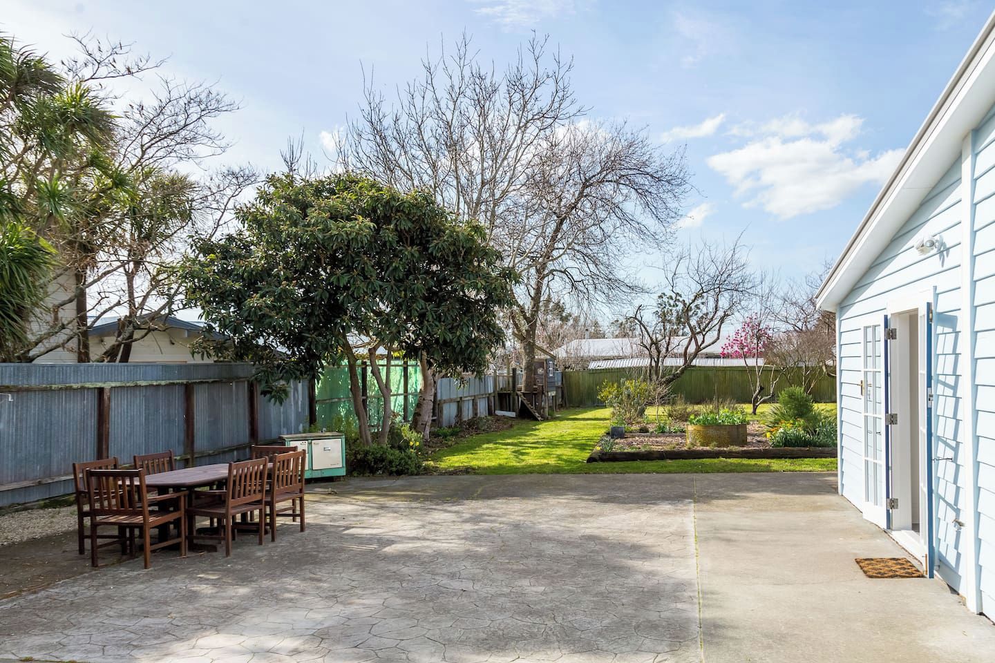 A backyard with a patio table and chairs, a fenced area, and a house in the background.