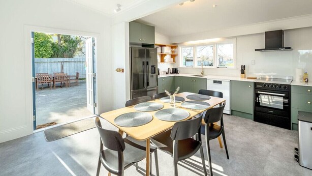 A modern kitchen with a dining area, featuring a large table with placemats, a refrigerator, oven, and a view of the backyard.