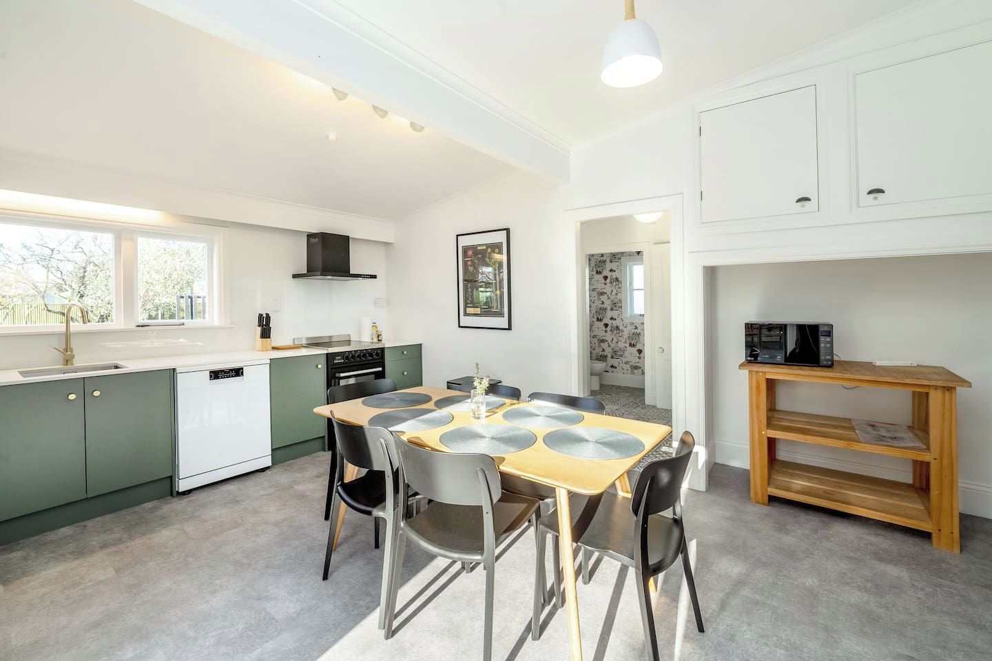 A modern kitchen with a dining area, featuring a central island, built-in appliances, and a view to the adjacent bathroom.