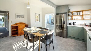 A modern kitchen with a stainless steel refrigerator, a dining area with a wooden table and chairs, and a built-in shelving unit with dishes and glasses.