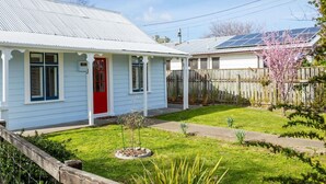 A single-story house with a red door, white siding, and a small front yard with a wooden fence and a tree.