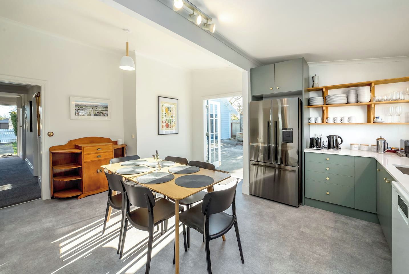 A modern kitchen with a stainless steel refrigerator, wooden cabinets, and a dining area with a table and chairs.
