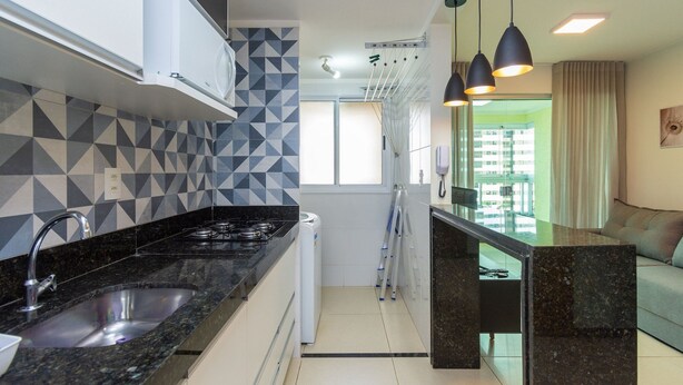 Una cocina moderna con encimera de granito negro, un lavabo empotrado y una estufa compacta. Se ve una ventana con vistas a un edificio.