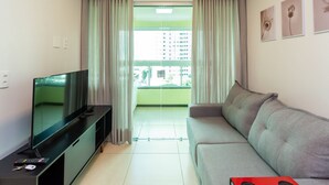 Una sala de estar con un televisor de pantalla plana sobre un soporte negro, un sofá gris y un objeto rojo en el suelo.