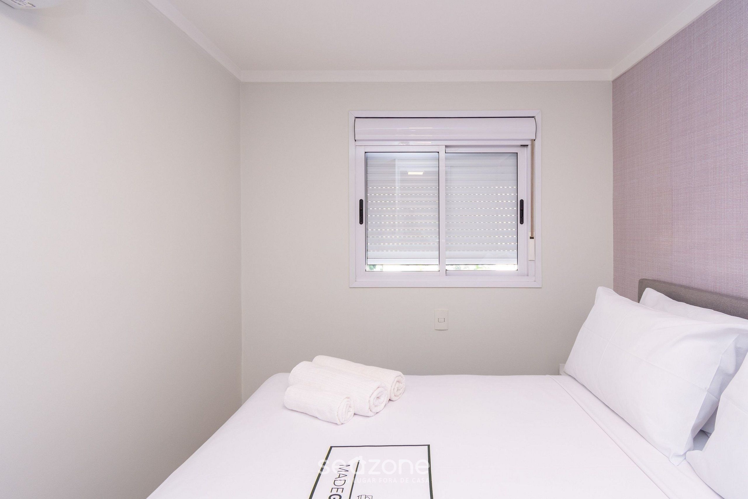 Una habitación de hotel con una cama individual, una ventana con persianas y una pared con un diseño texturizado.