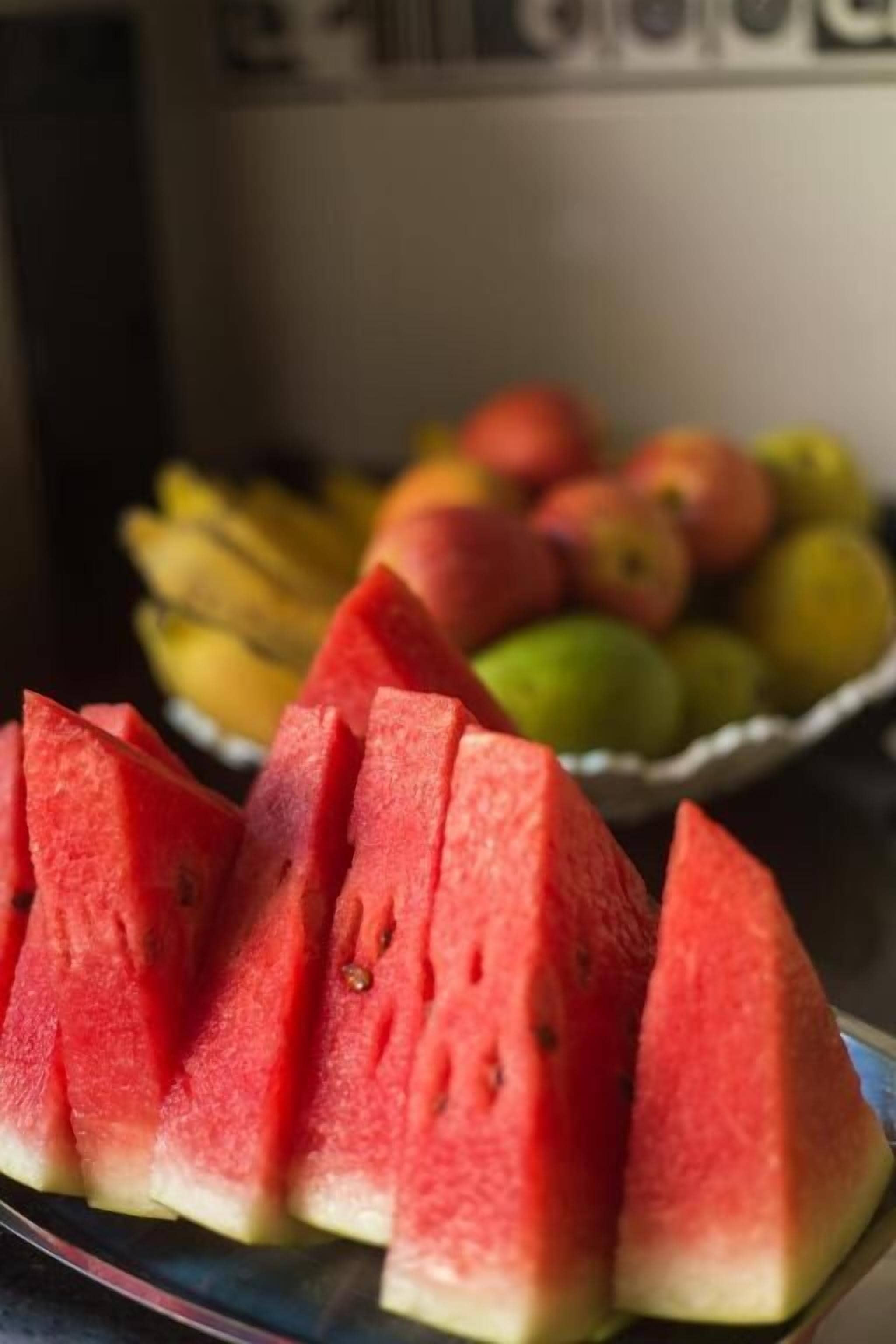 A plate of watermelon slices on a table with a bowl of mixed fruits in the background.