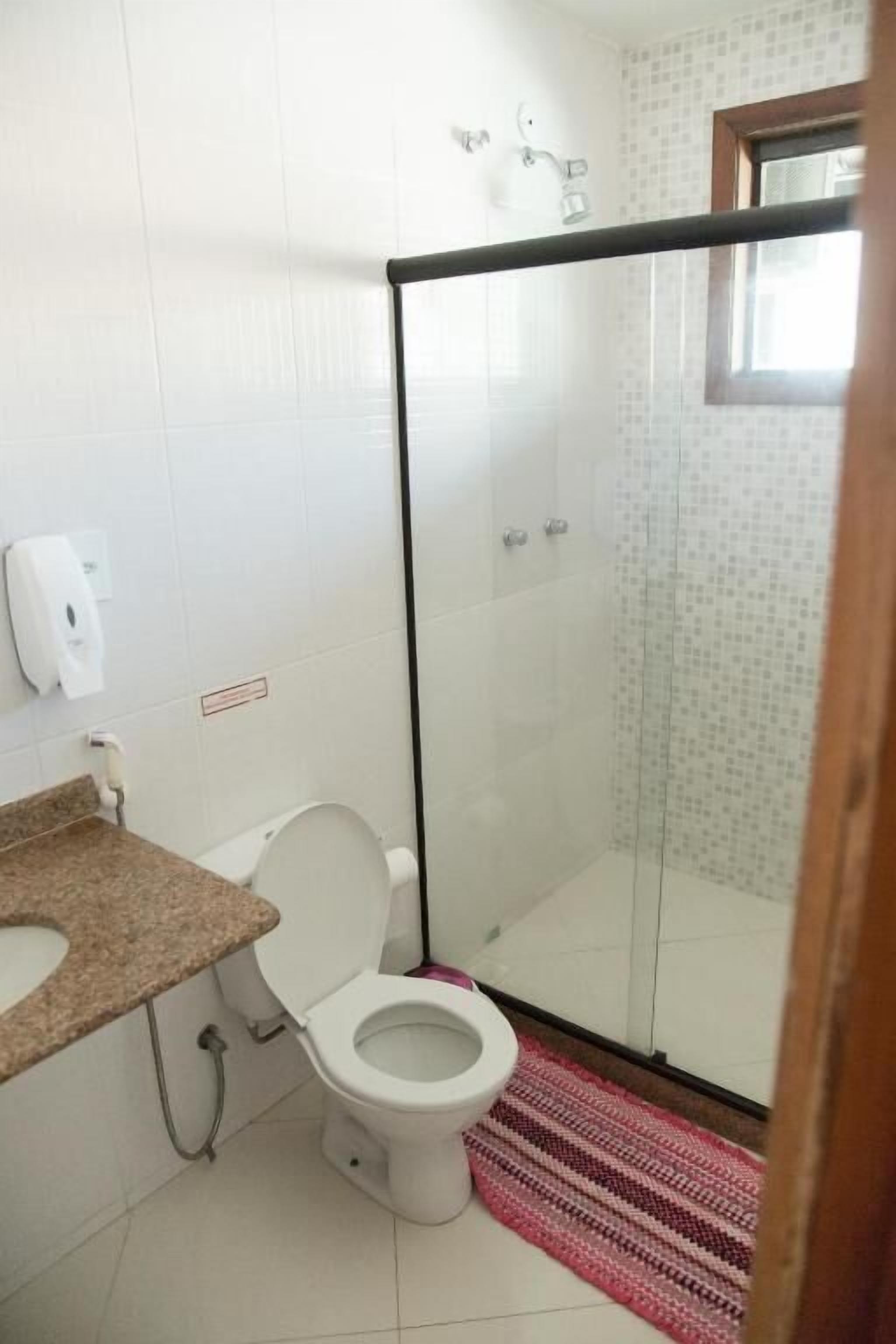Een badkamer met toilet, douchecabine en wastafel met zeepdispenser.