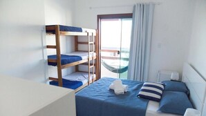 A room with bunk beds, a bed with blue bedding, a hammock, and a view through a glass door. - Enseada Hostel (Arraial do Cabo)