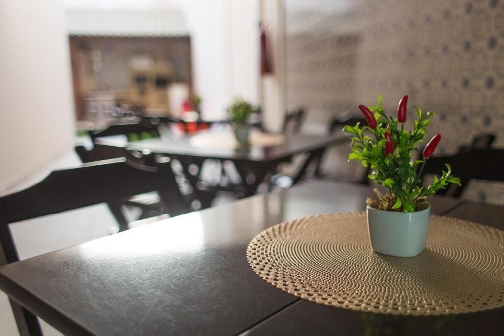 Een eettafel met een geweven placemat en een potplant met rode bladeren.