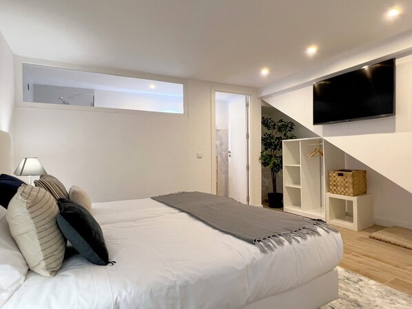 Un dormitorio moderno con una cama grande, un televisor montado en la pared y una escalera que lleva a un nivel superior.