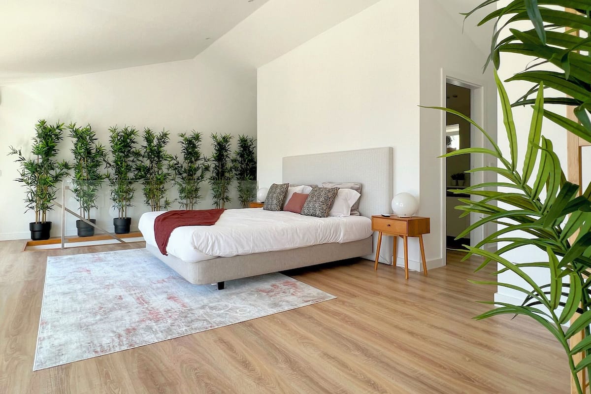 A modern bedroom with a large bed, a wooden floor, and multiple potted plants.