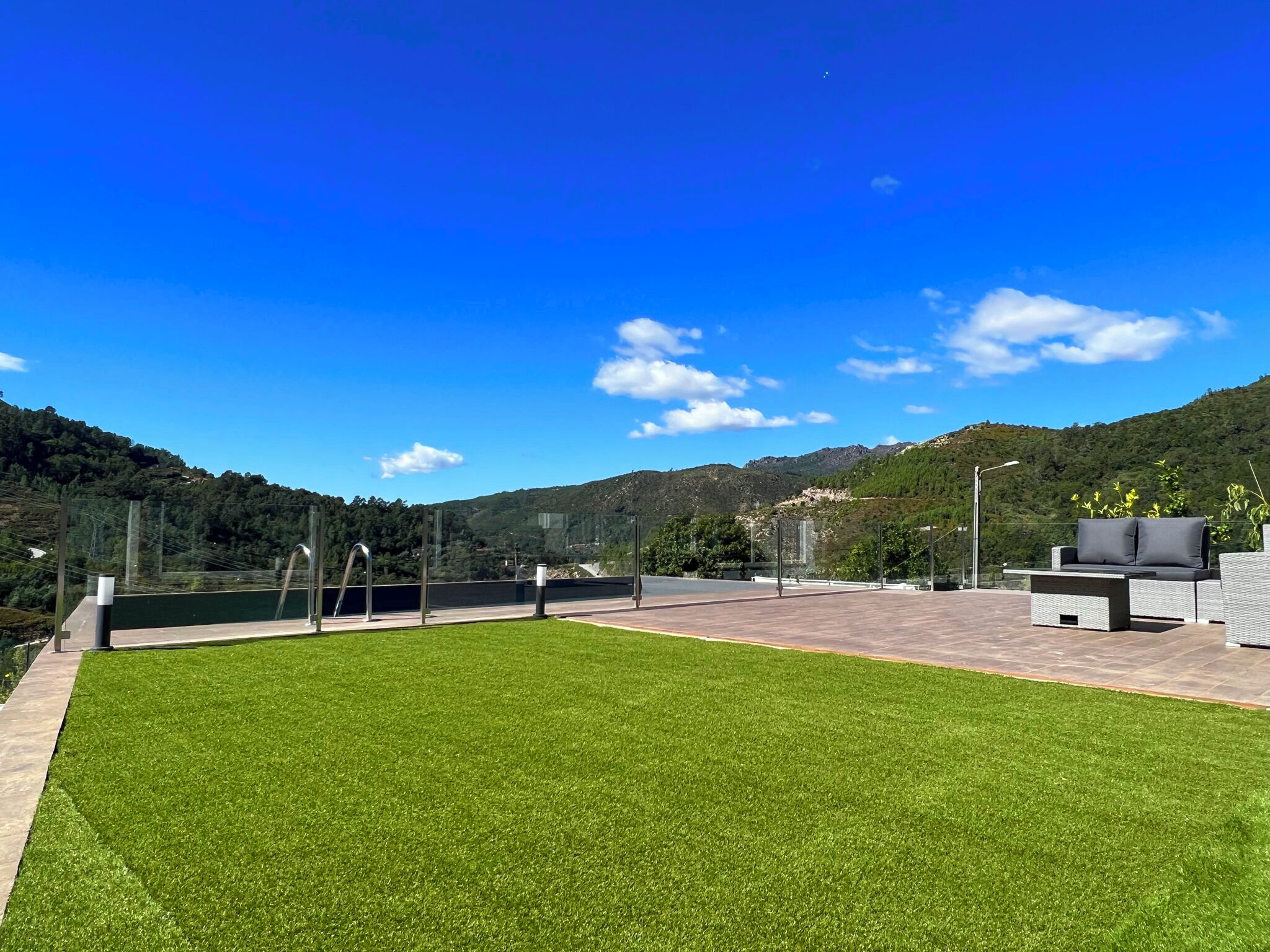A rooftop terrace with a well-maintained lawn, outdoor furniture, and a scenic mountain backdrop.