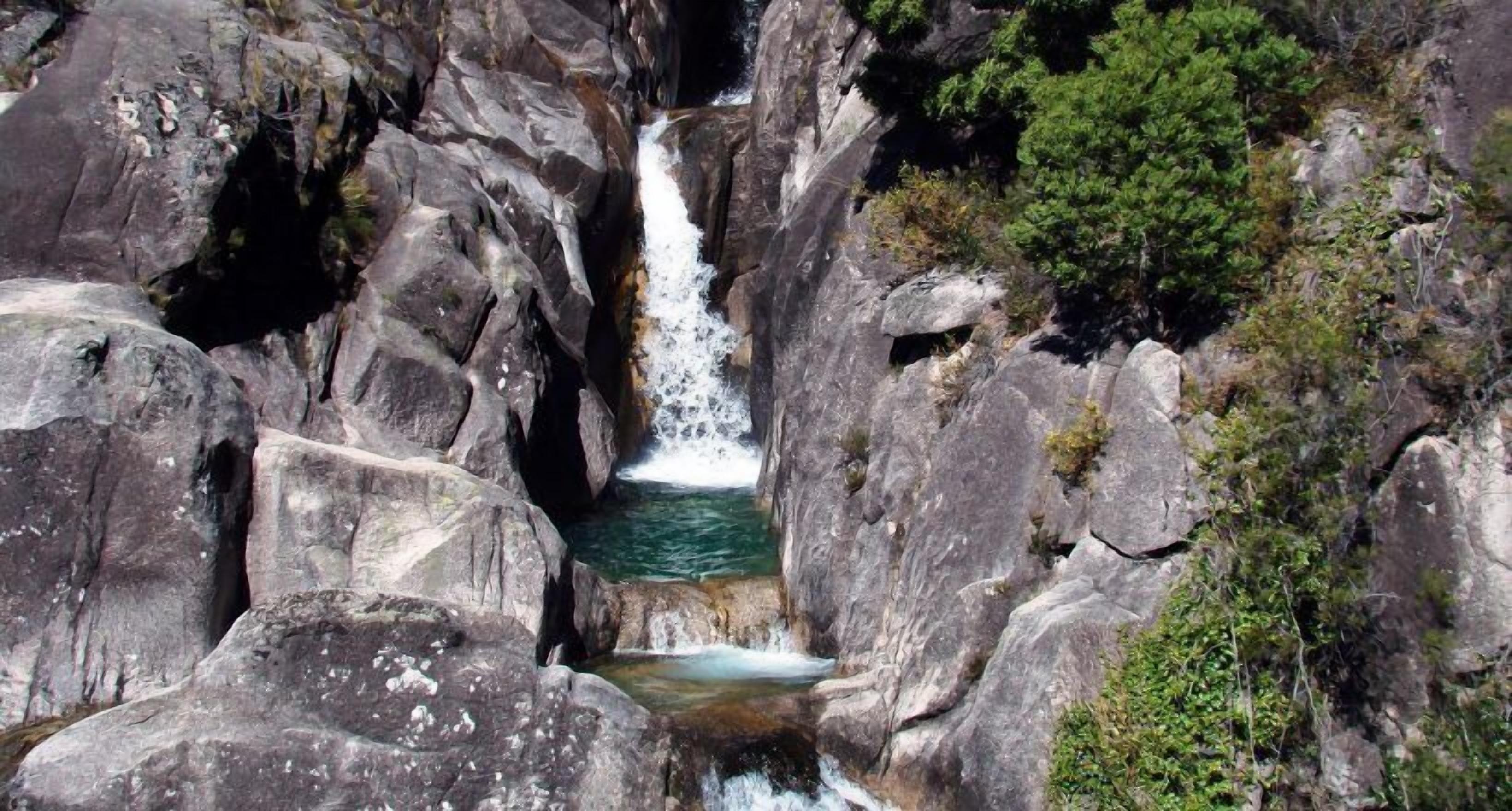 A waterfall cascading through a rocky gorge with dense foliage on the right.