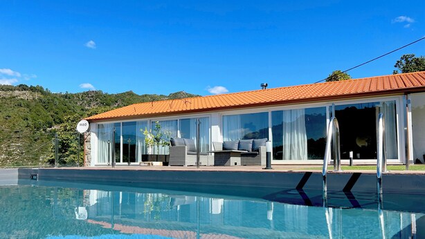 A modern house with a swimming pool, large windows, and a patio with outdoor furniture.