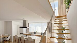 A modern kitchen with a central island, wooden staircase, and potted plants.