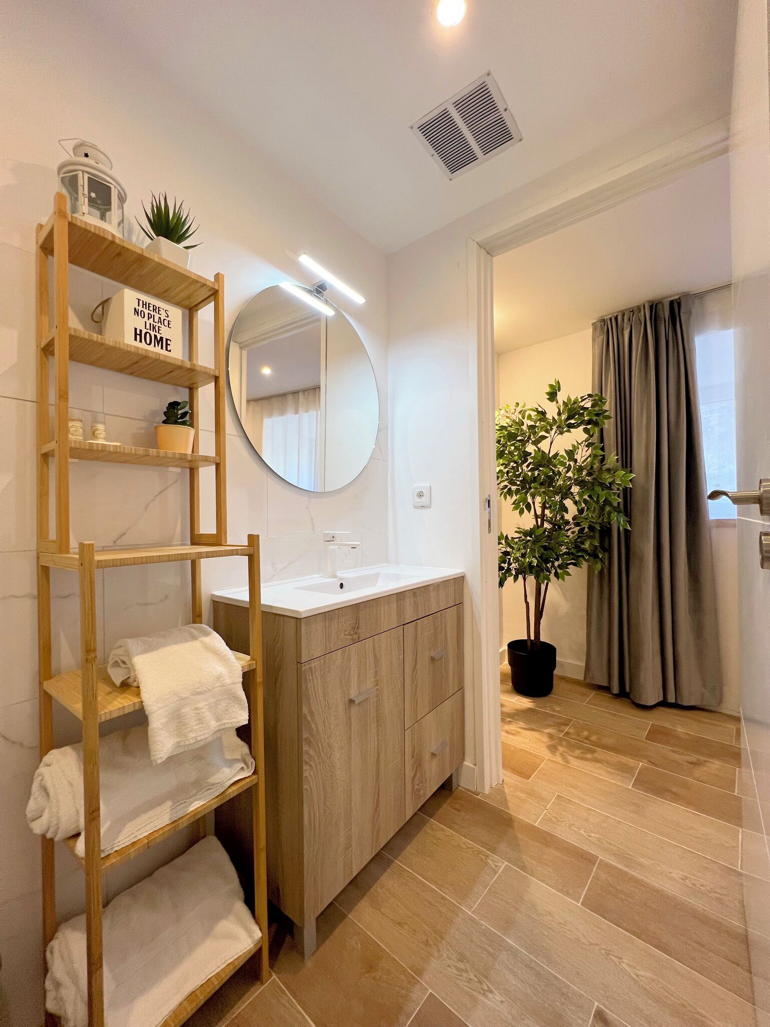 A modern bathroom with a wooden vanity, a round mirror, and a shelf with towels.