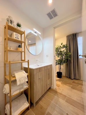 Un bagno moderno con un mobile bagno in legno, uno specchio rotondo e uno scaffale con asciugamani.