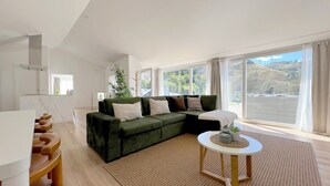 A modern living room with a green sectional sofa, a small round table, and a large window offering a view of the outdoors.