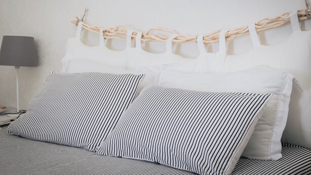 Un lit avec une literie à rayures, une tête de lit blanche ornée de motifs en forme de corde et une lampe de chevet.