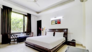 A hotel room with a large bed, a desk, a chair, a small table, and a ceiling fan. - Blue Moon Residency Hotel & Restaurant (Gurugram)