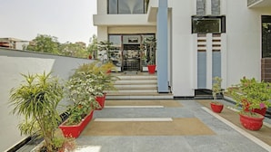 A modern building entrance with a paved pathway, potted plants, and a visible door. - Blue Moon Residency Hotel & Restaurant (Gurugram)
