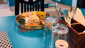 A dining area with a table set for a meal, including a metal tray with food, glasses, and cutlery. - Blue Moon Residency Hotel & Restaurant (Gurugram)