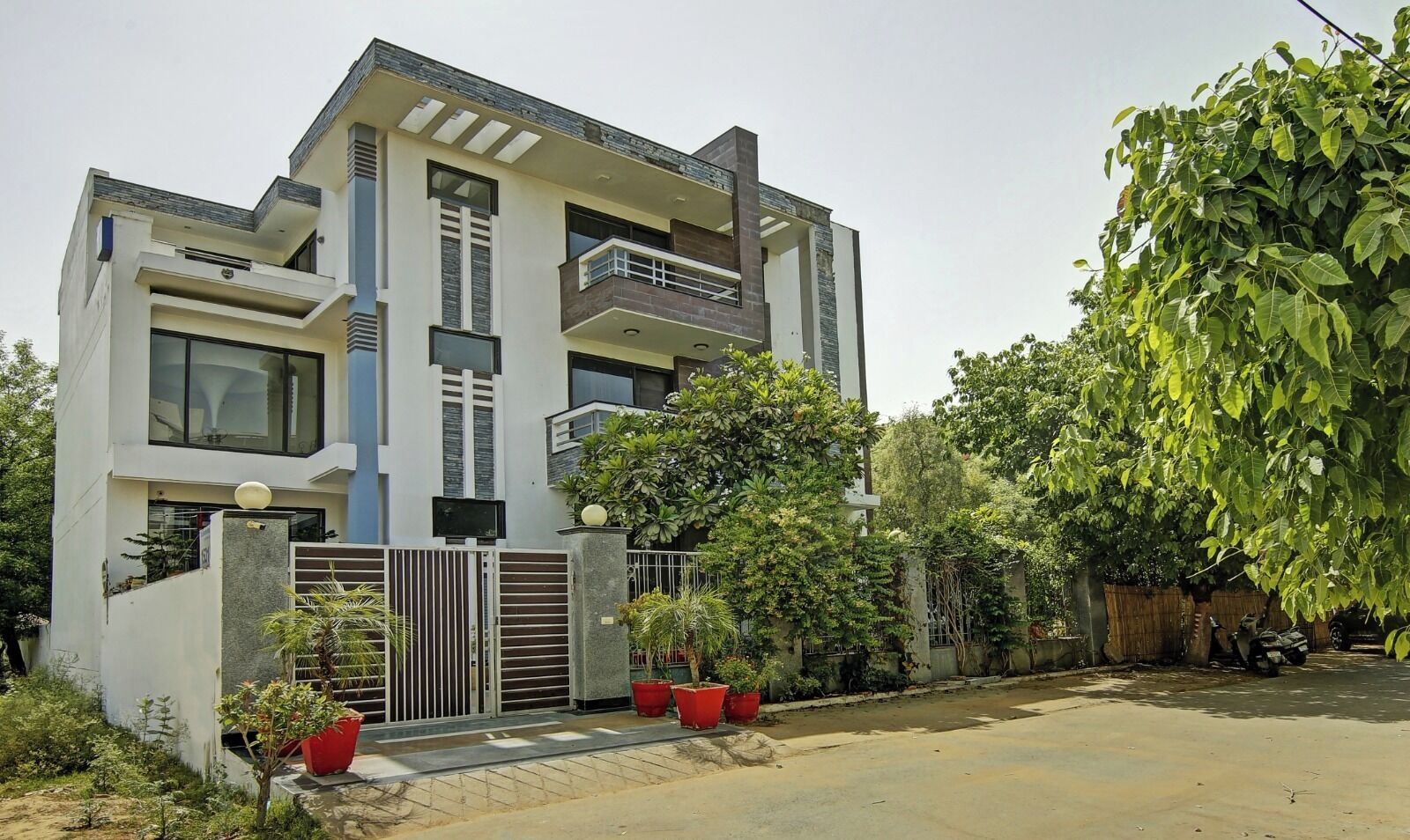 A modern two-story house with a balcony, a gated entrance, and potted plants.